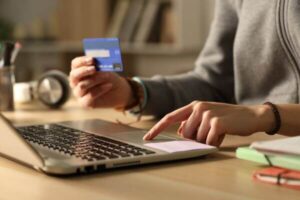 Student hands with credit card on laptop at night.